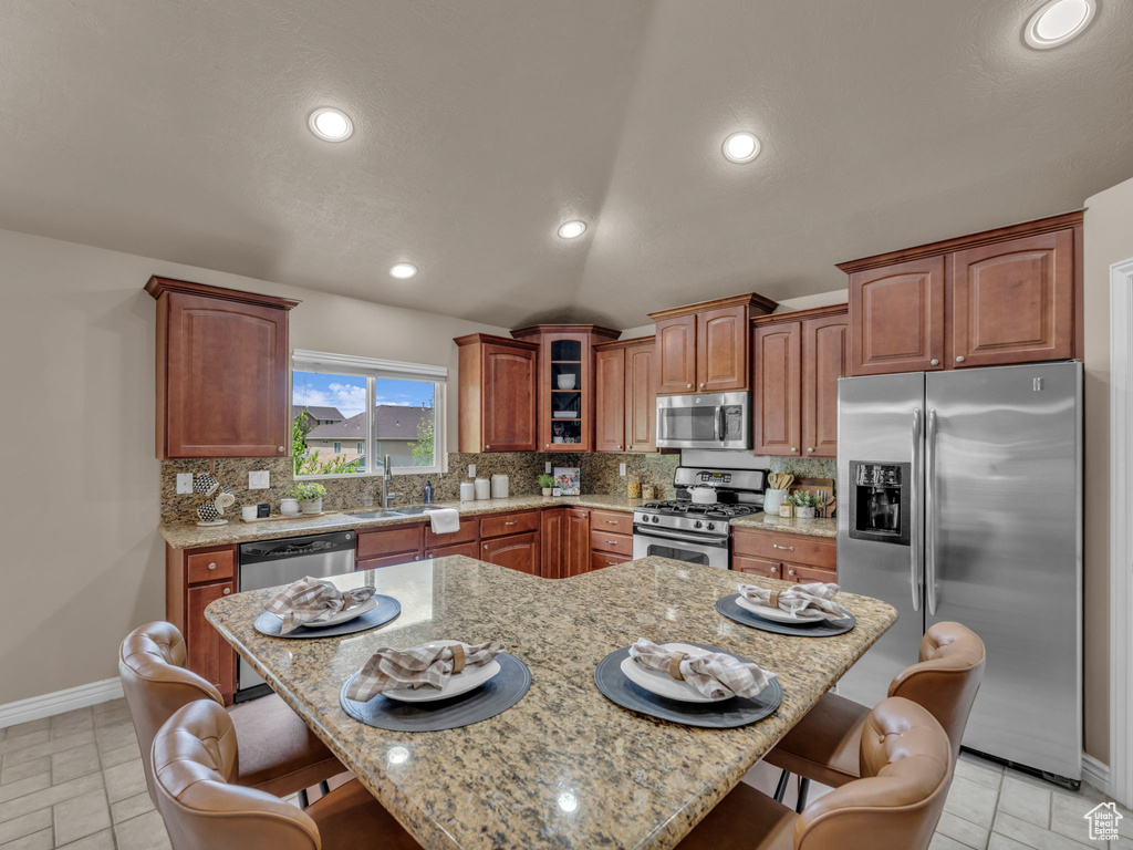 Kitchen featuring appliances with stainless steel finishes, a kitchen breakfast bar, tasteful backsplash, baseboards, and a sink