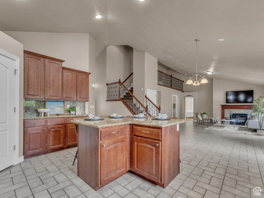 Kitchen with lofted ceiling, open floor plan, a kitchen island with sink, light stone counters, and tasteful backsplash