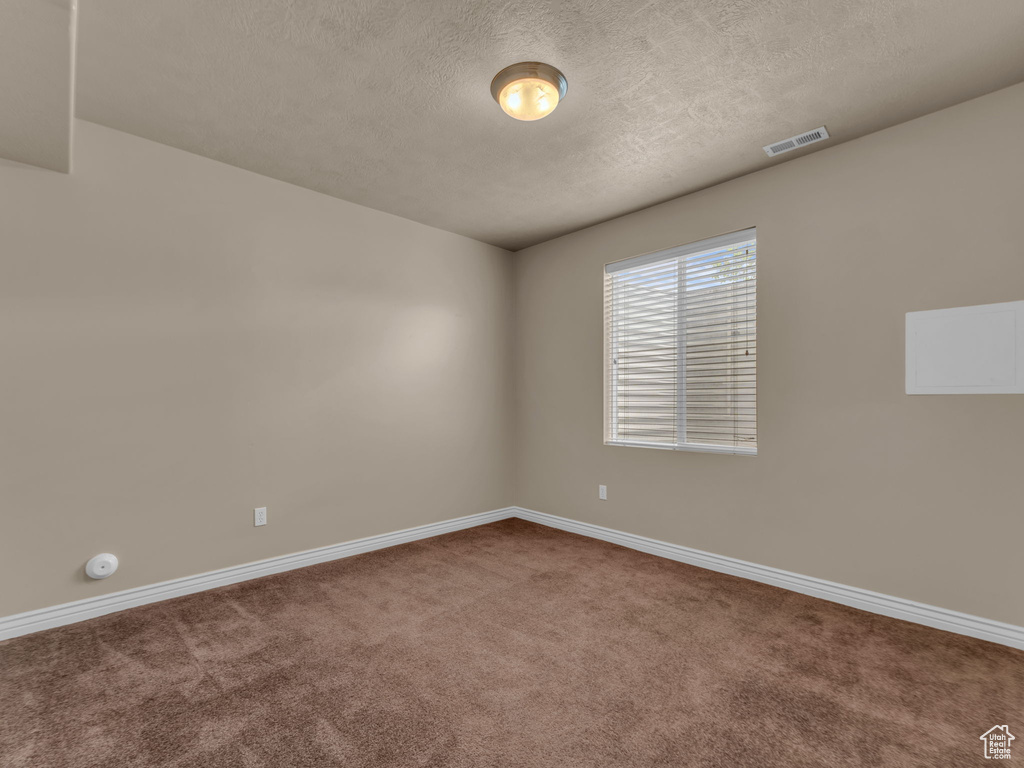 Empty room featuring baseboards, a textured ceiling, and carpet floors