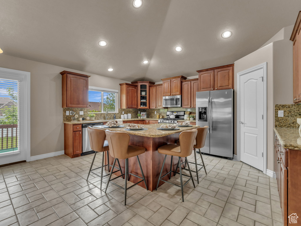 Kitchen featuring appliances with stainless steel finishes, tasteful backsplash, a breakfast bar, light stone countertops, and a kitchen island