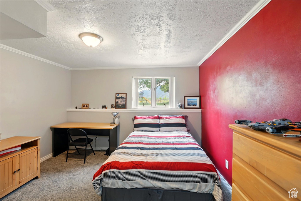 Carpeted bedroom featuring a textured ceiling, ornamental molding, baseboards, and a desk
