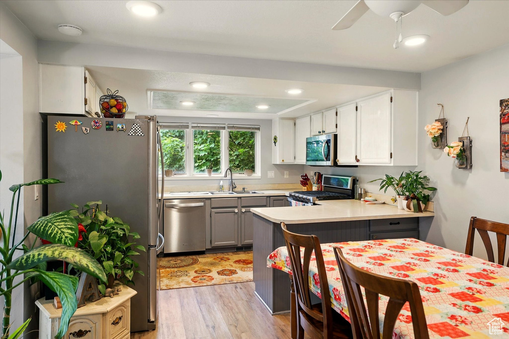 Kitchen featuring appliances with stainless steel finishes, a sink, a peninsula, light wood-style floors, and light countertops