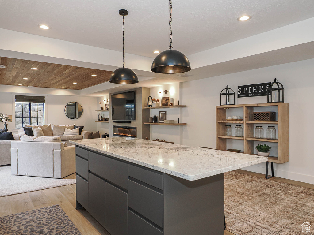 Kitchen with decorative light fixtures, a center island, light wood-type flooring, recessed lighting, and light stone countertops