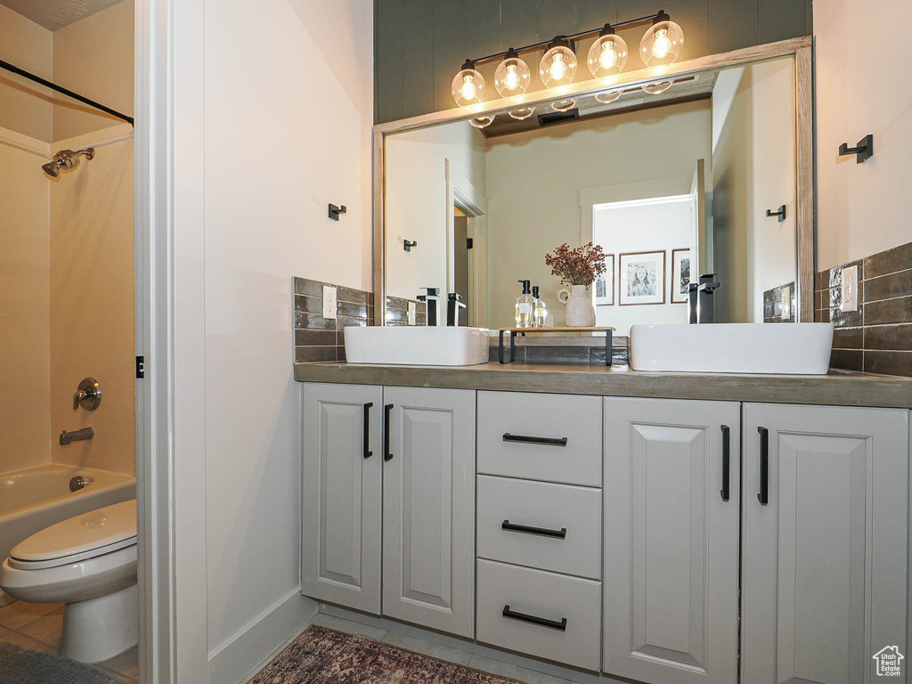 Bathroom with double vanity, shower / tub combination, toilet, tile patterned floors, and baseboards