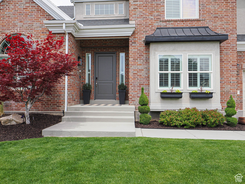 Doorway to property featuring a standing seam roof, a lawn, and brick siding