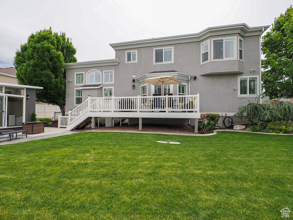 Rear view of property featuring stucco siding, a deck, a patio, and a lawn