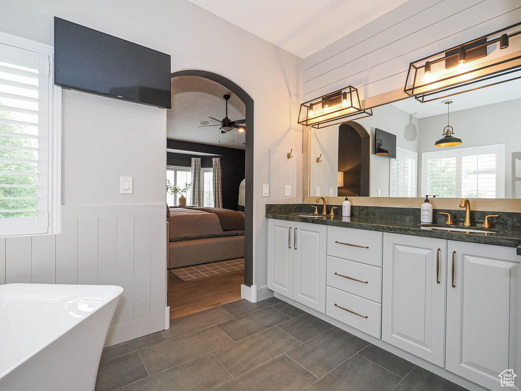 Full bathroom with ceiling fan, ensuite bath, double vanity, plenty of natural light, and wainscoting