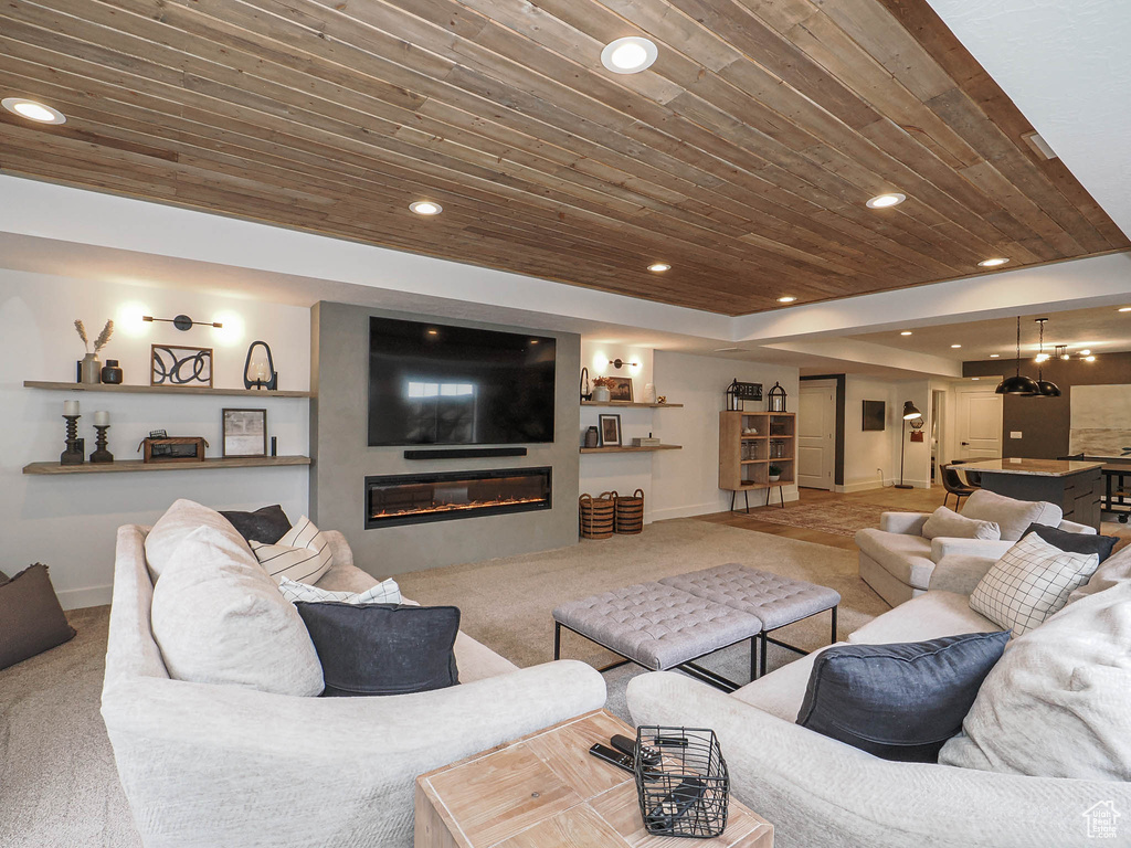 Living room featuring carpet floors, wood ceiling, baseboards, recessed lighting, and a glass covered fireplace