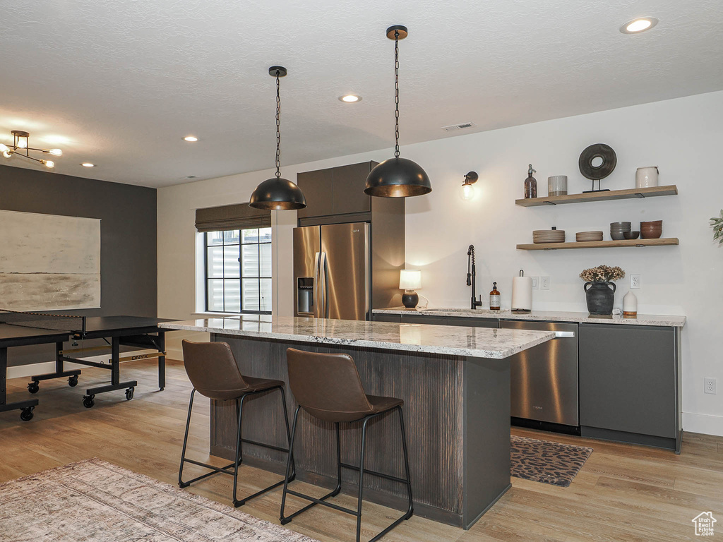 Kitchen with stainless steel appliances, a sink, light wood-type flooring, a kitchen bar, and recessed lighting