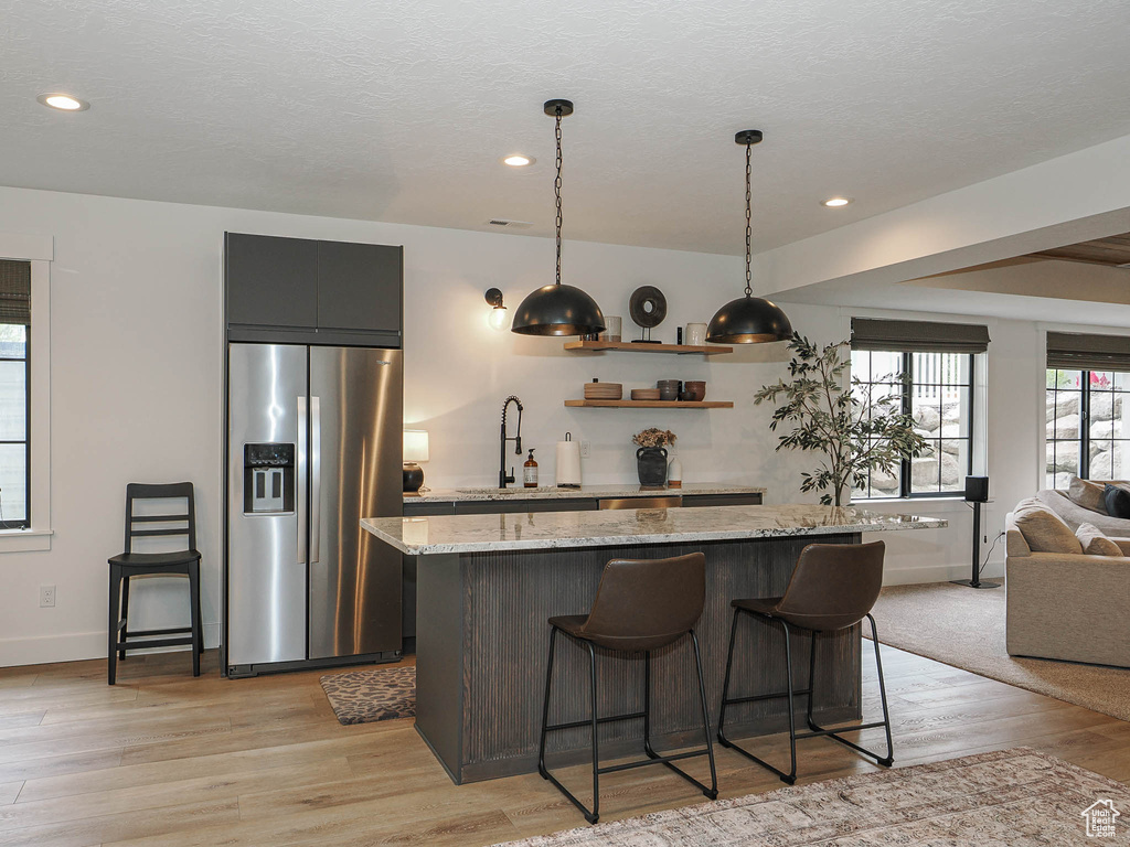 Kitchen featuring stainless steel fridge with ice dispenser, a kitchen island, open floor plan, light wood-style flooring, and a breakfast bar