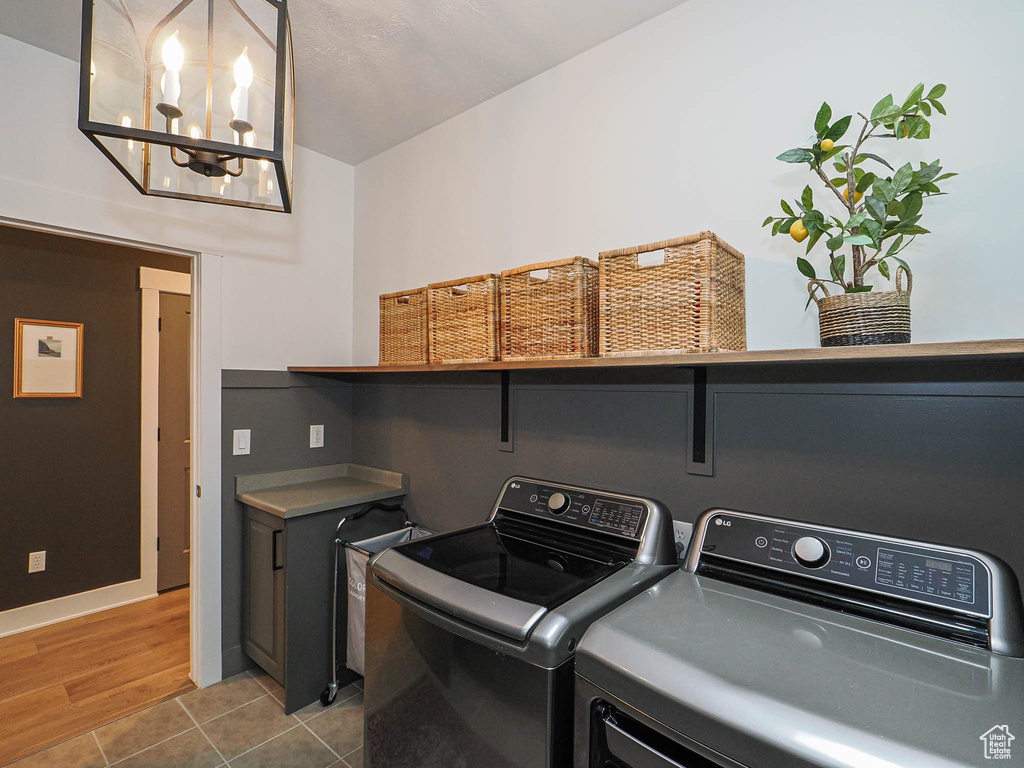 Clothes washing area featuring washer and dryer, a chandelier, and tile patterned flooring