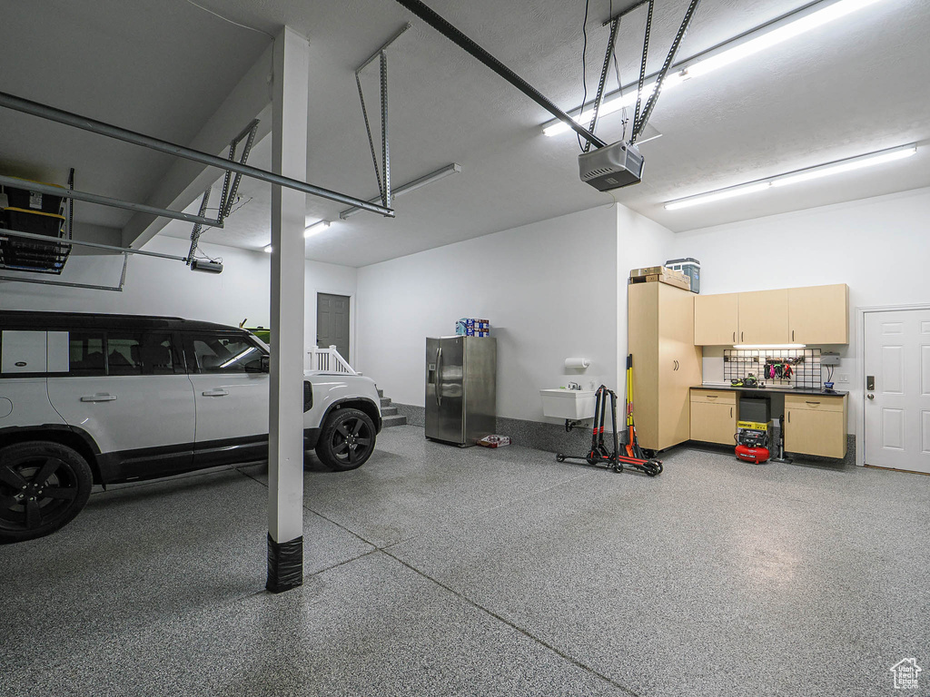 Garage featuring a garage door opener and stainless steel fridge