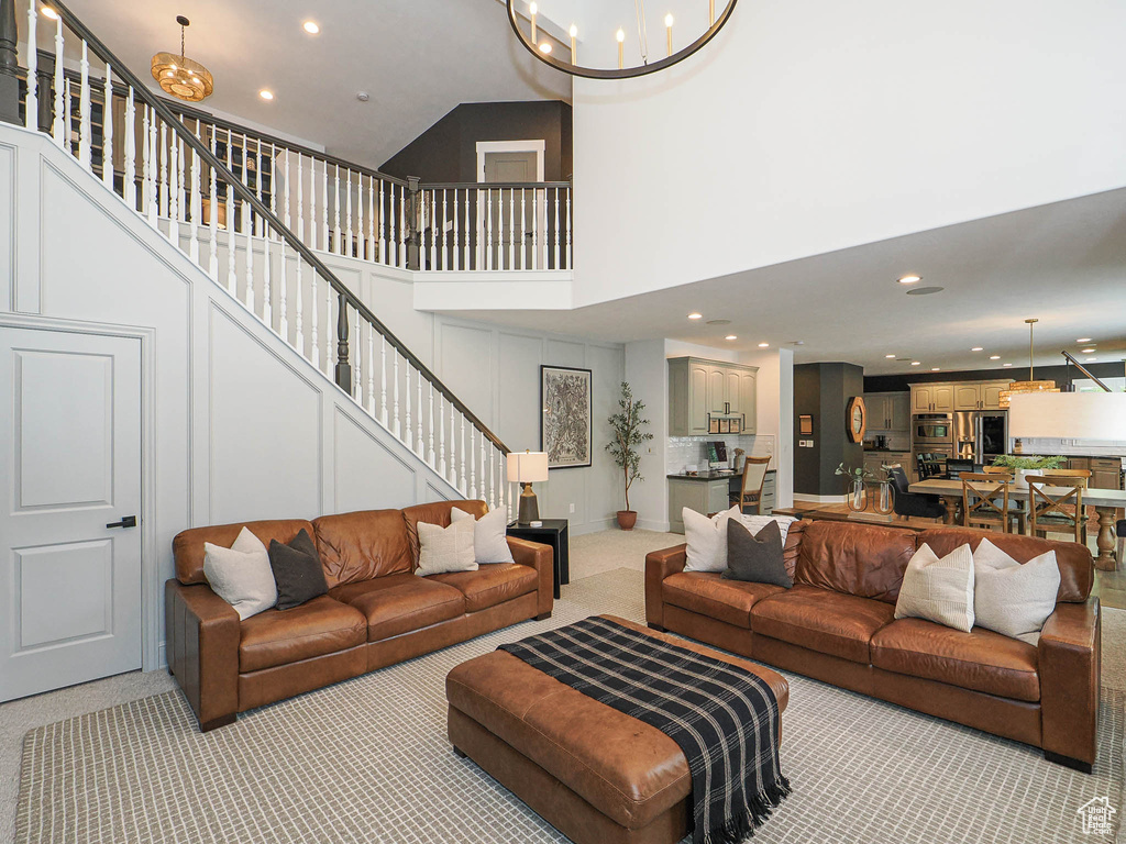 Living area featuring a chandelier, light colored carpet, stairs, recessed lighting, and a towering ceiling
