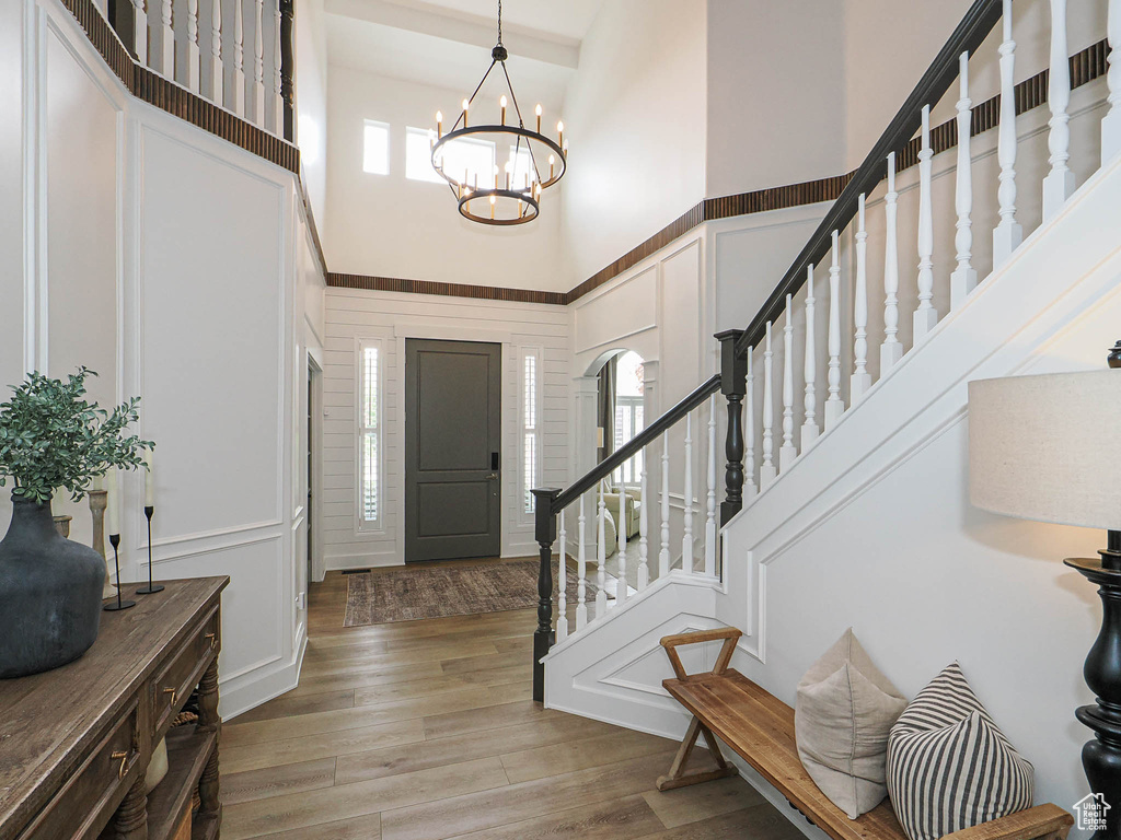 Entryway with a high ceiling, a decorative wall, stairs, a chandelier, and light wood-type flooring