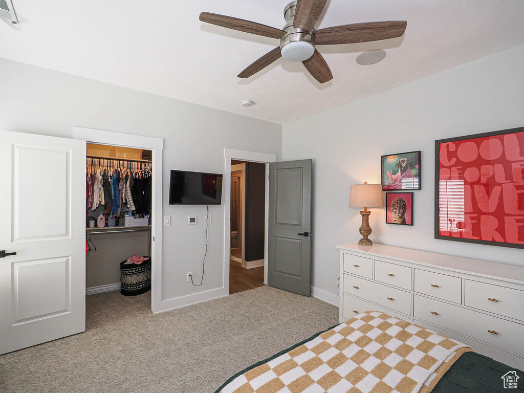 Carpeted bedroom featuring a walk in closet, a closet, baseboards, and ceiling fan