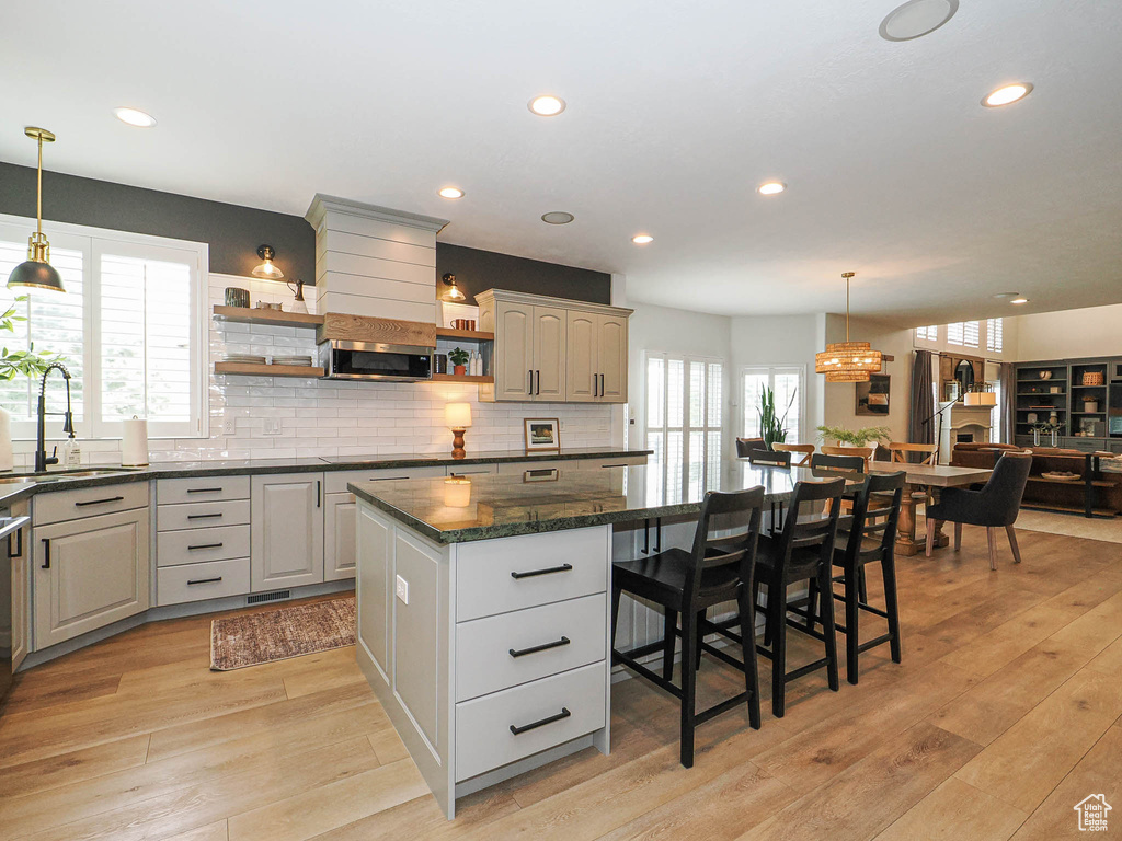 Kitchen featuring a sink, open shelves, a kitchen island, stainless steel microwave, and light wood finished floors