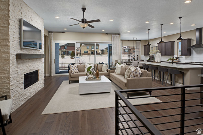 Living area with a ceiling fan, dark wood-style flooring, recessed lighting, a fireplace, and a textured ceiling
