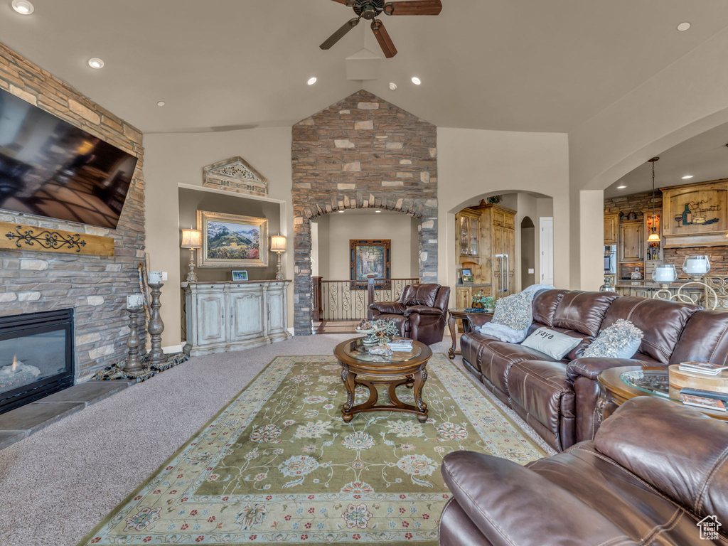 Living area featuring arched walkways, a ceiling fan, a stone fireplace, carpet, and recessed lighting