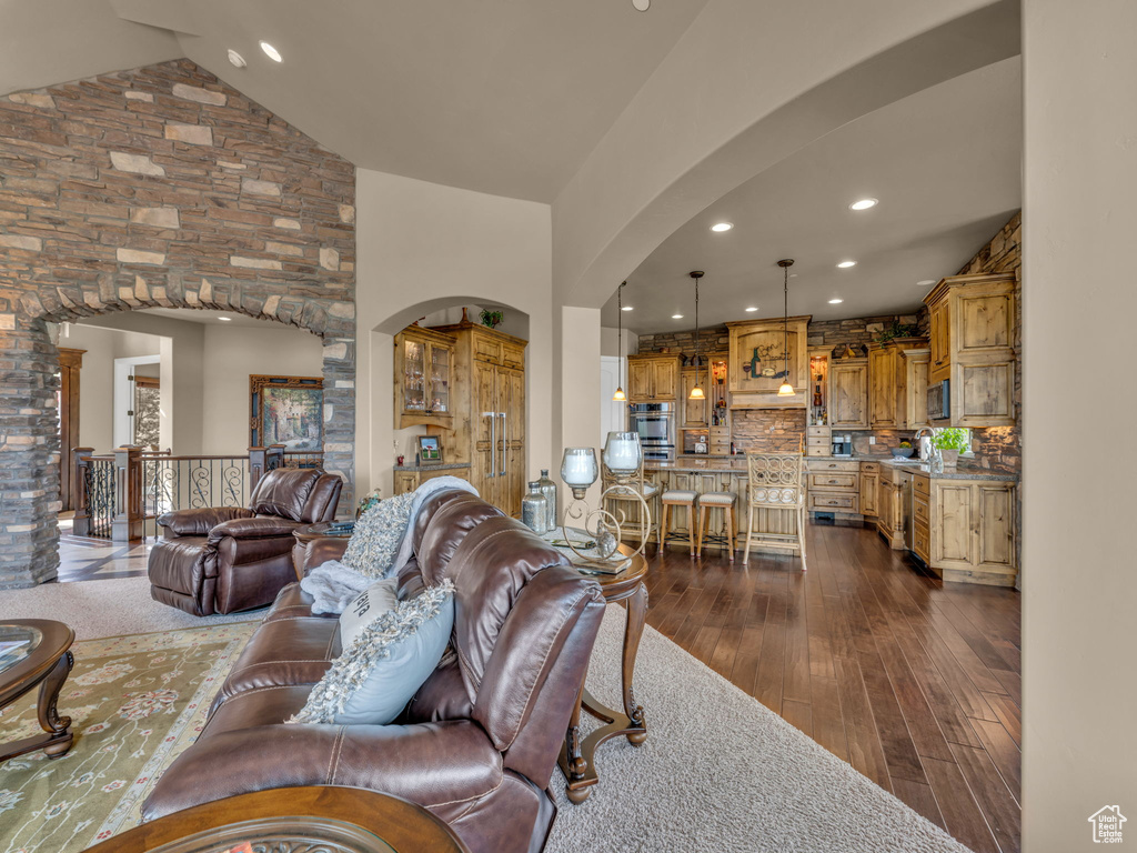 Living area featuring arched walkways, dark wood-type flooring, recessed lighting, and high vaulted ceiling
