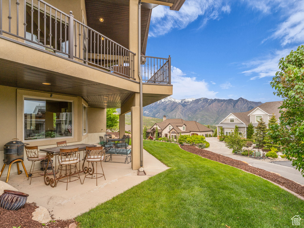 View of grassy yard featuring a balcony, a mountain view, a patio area, and a residential view