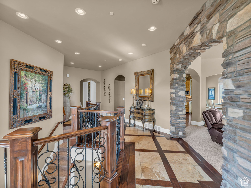 Hallway with arched walkways, an upstairs landing, recessed lighting, inlaid floor details, and baseboards