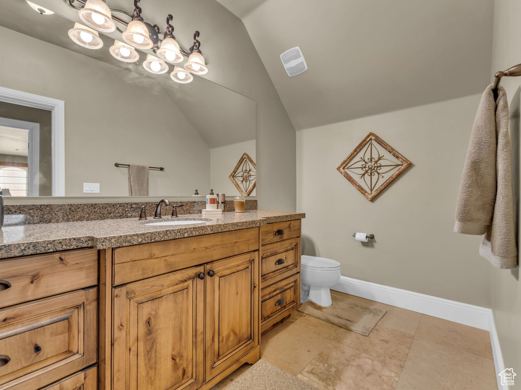 Bathroom with vanity, toilet, vaulted ceiling, and baseboards