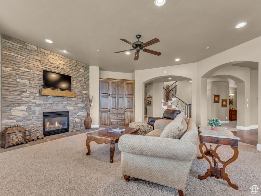 Carpeted living room with ceiling fan, a stone fireplace, arched walkways, stairway, and recessed lighting
