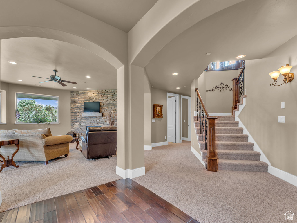Living area featuring ceiling fan, dark wood finished floors, stairs, a fireplace, and arched walkways