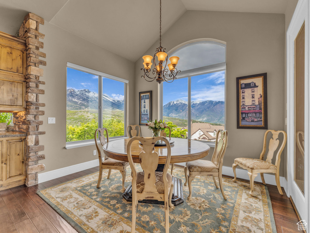 Dining area featuring a chandelier, lofted ceiling, dark wood-style flooring, a mountain view, and baseboards