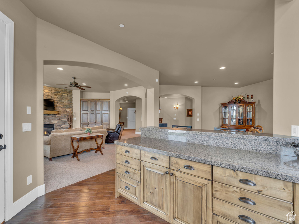 Kitchen featuring arched walkways, a ceiling fan, a fireplace, dark wood finished floors, and light stone countertops