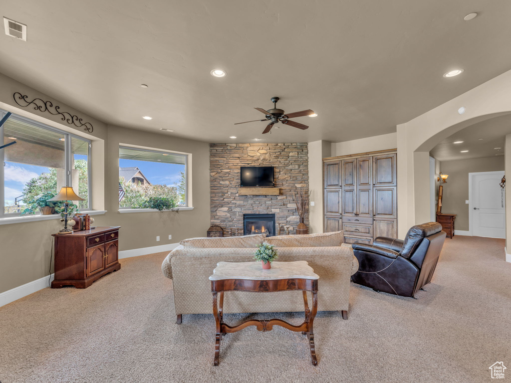 Living area with ceiling fan, arched walkways, baseboards, a fireplace, and light colored carpet