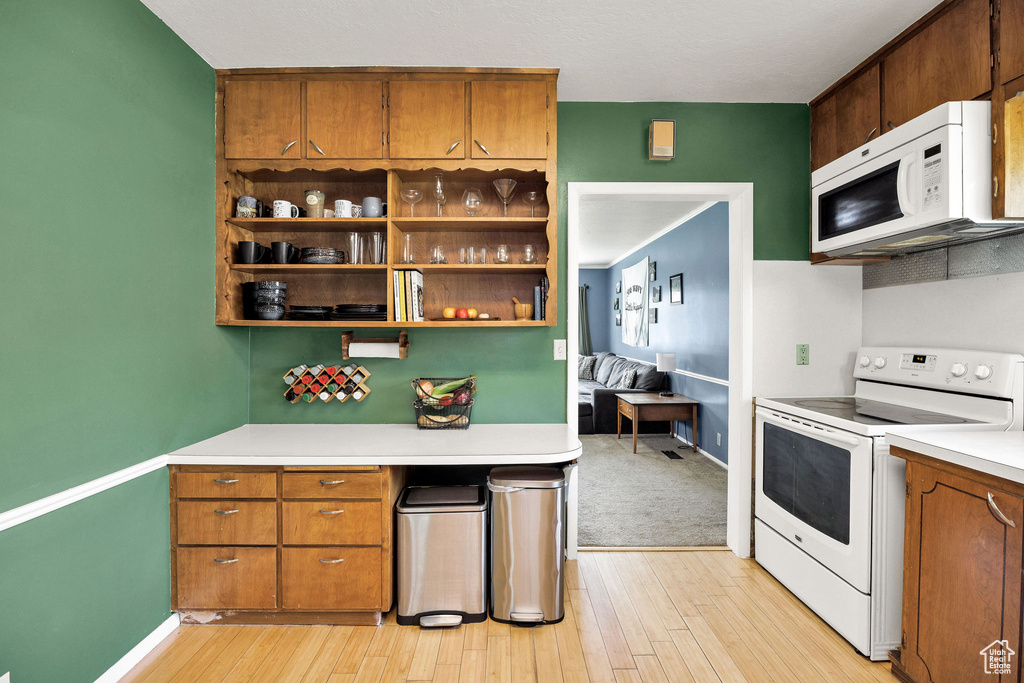 Kitchen with white appliances, light countertops, light wood finished floors, open shelves, and brown cabinetry