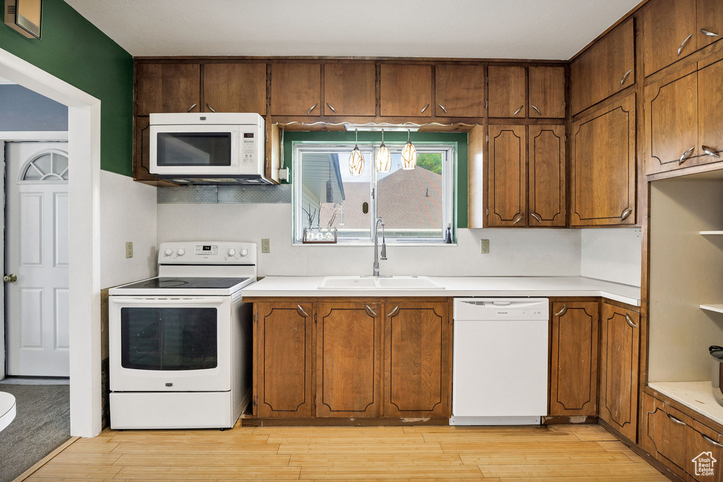 Kitchen with white appliances, a sink, light wood-style flooring, and light countertops