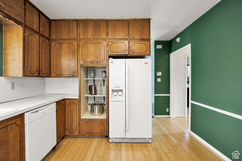 Kitchen featuring white appliances, light wood finished floors, light countertops, and brown cabinetry