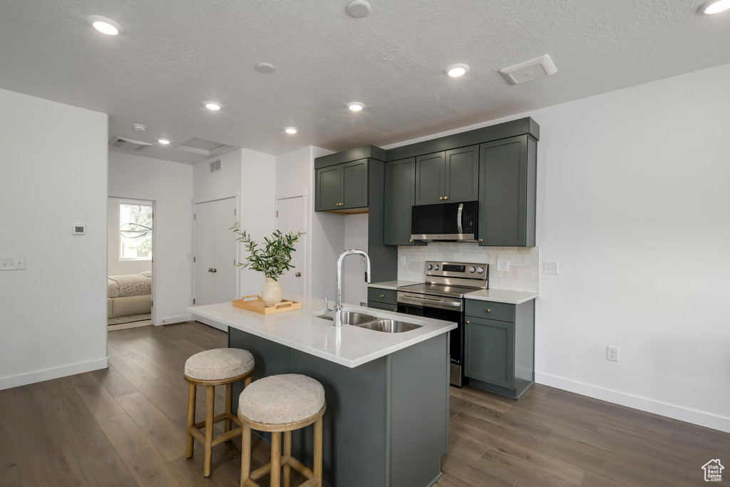 Kitchen with stainless steel appliances, a sink, baseboards, dark wood-type flooring, and backsplash