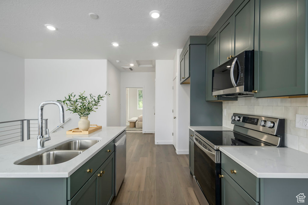 Kitchen featuring stainless steel appliances, a sink, decorative backsplash, dark wood finished floors, and light countertops