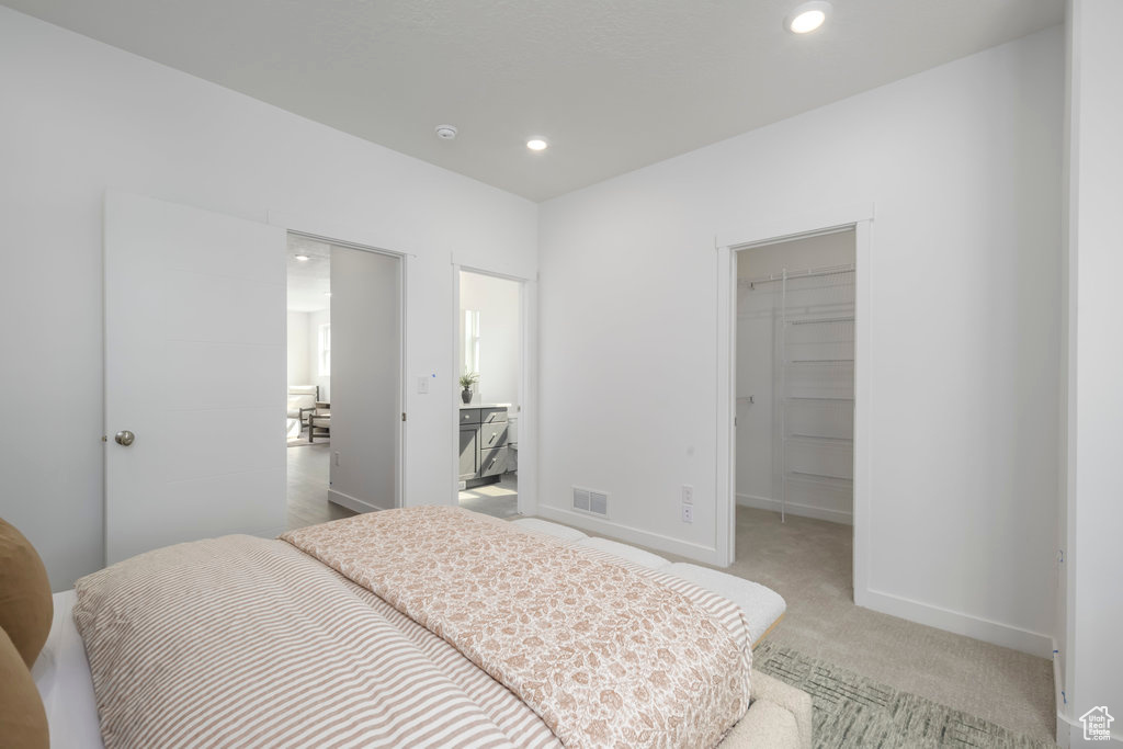 Bedroom with a spacious closet, baseboards, light colored carpet, recessed lighting, and a closet