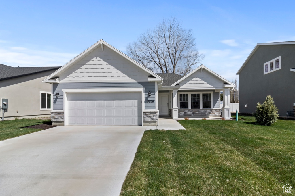 View of front facade featuring a garage, concrete driveway, a front lawn, stone siding, and a porch
