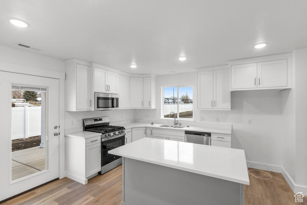 Kitchen with appliances with stainless steel finishes, a sink, white cabinetry, light wood-type flooring, and recessed lighting