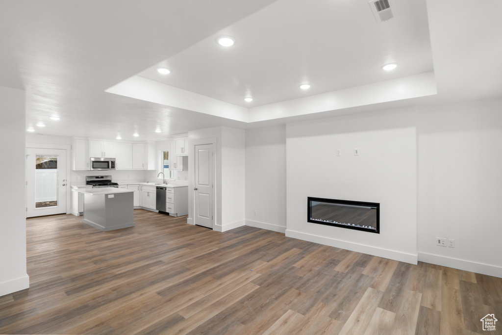 Unfurnished living room featuring a tray ceiling, recessed lighting, baseboards, dark wood-style flooring, and a glass covered fireplace