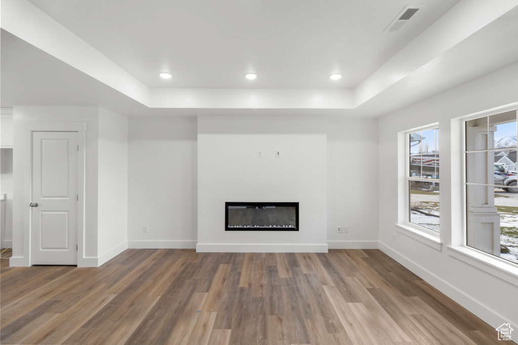 Unfurnished living room with a raised ceiling, wood finished floors, a glass covered fireplace, baseboards, and recessed lighting