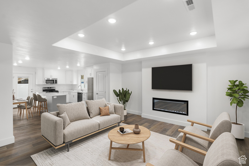 Living area with a tray ceiling, baseboards, dark wood finished floors, recessed lighting, and a glass covered fireplace