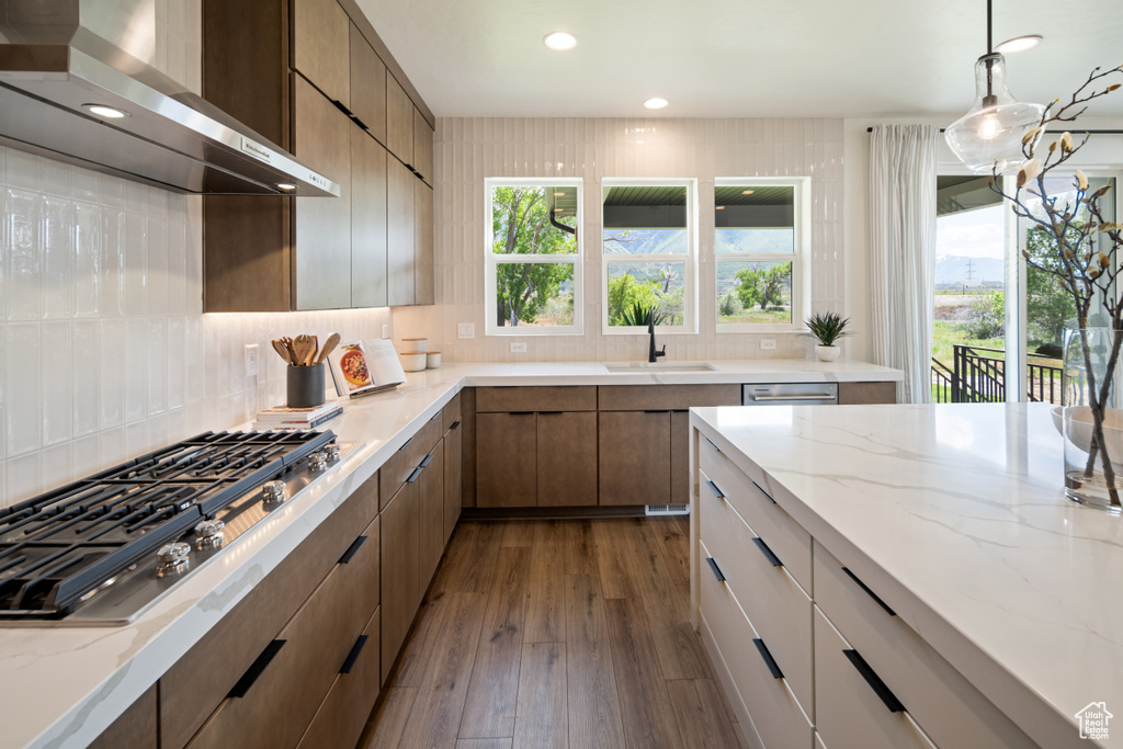 Kitchen with wall chimney range hood, a sink, stainless steel gas stovetop, backsplash, and recessed lighting