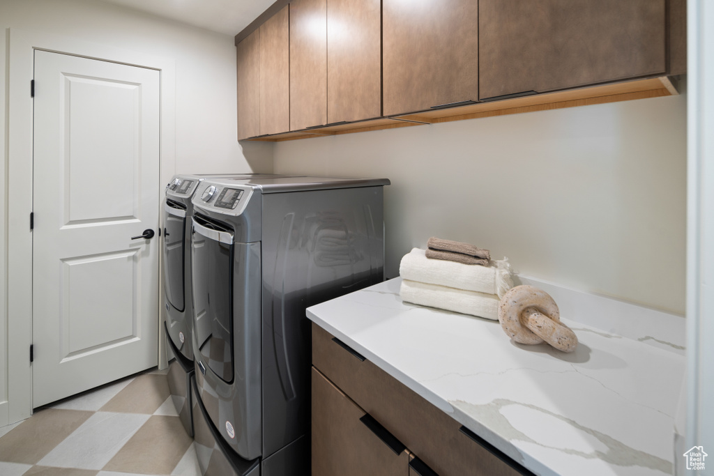 Clothes washing area featuring cabinet space, washer and clothes dryer, and light floors