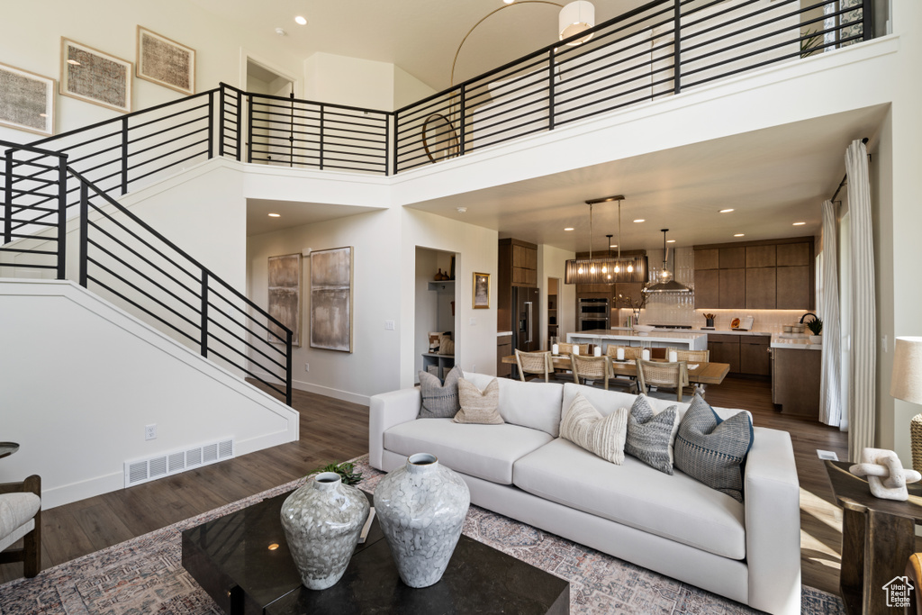 Living room with dark wood-style floors, stairs, baseboards, a high ceiling, and recessed lighting