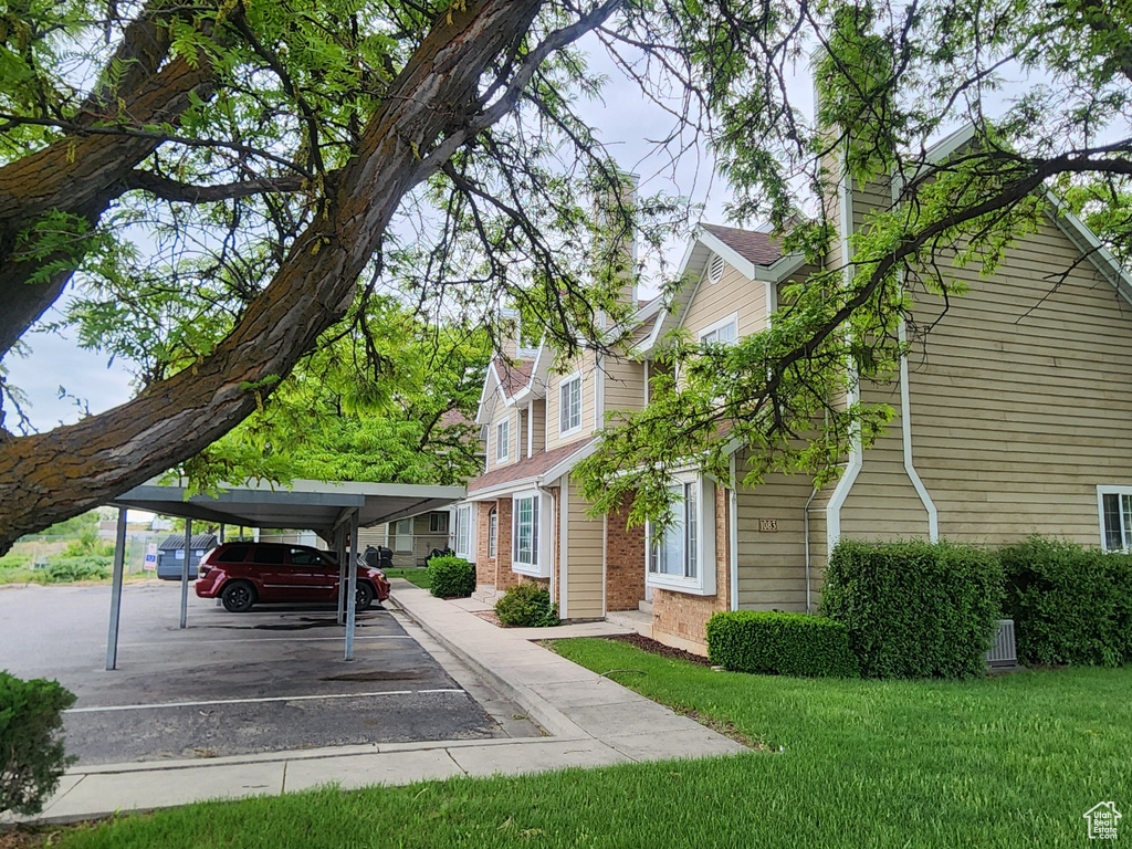 View of home\\\\\\\\\\\\\\\'s exterior featuring a chimney, covered parking, brick siding, and a lawn