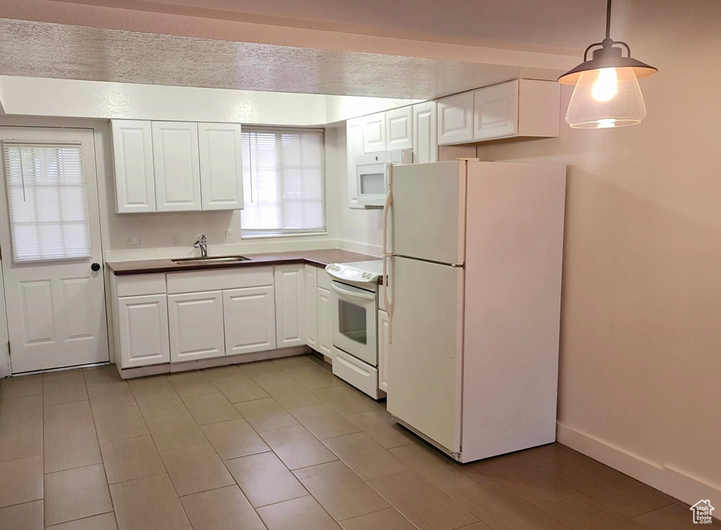Kitchen with white appliances, a sink, white cabinetry, decorative light fixtures, and baseboards