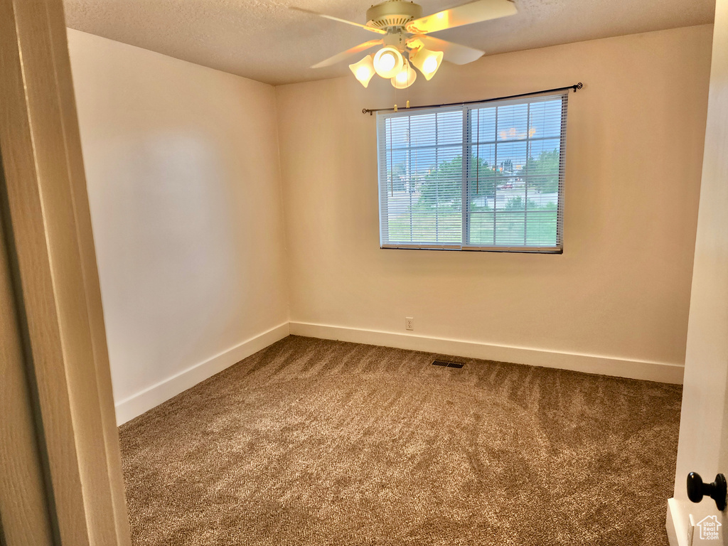 Empty room featuring carpet flooring, baseboards, a ceiling fan, and a textured ceiling