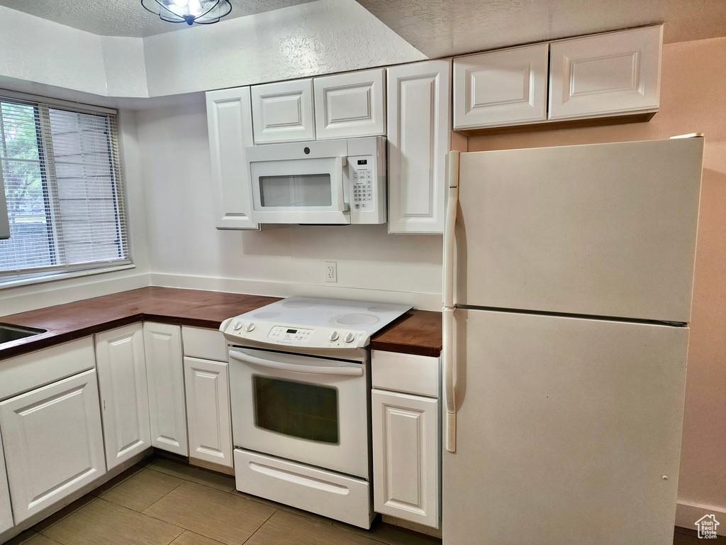 Kitchen featuring white appliances, wooden counters, white cabinetry, and tile patterned flooring