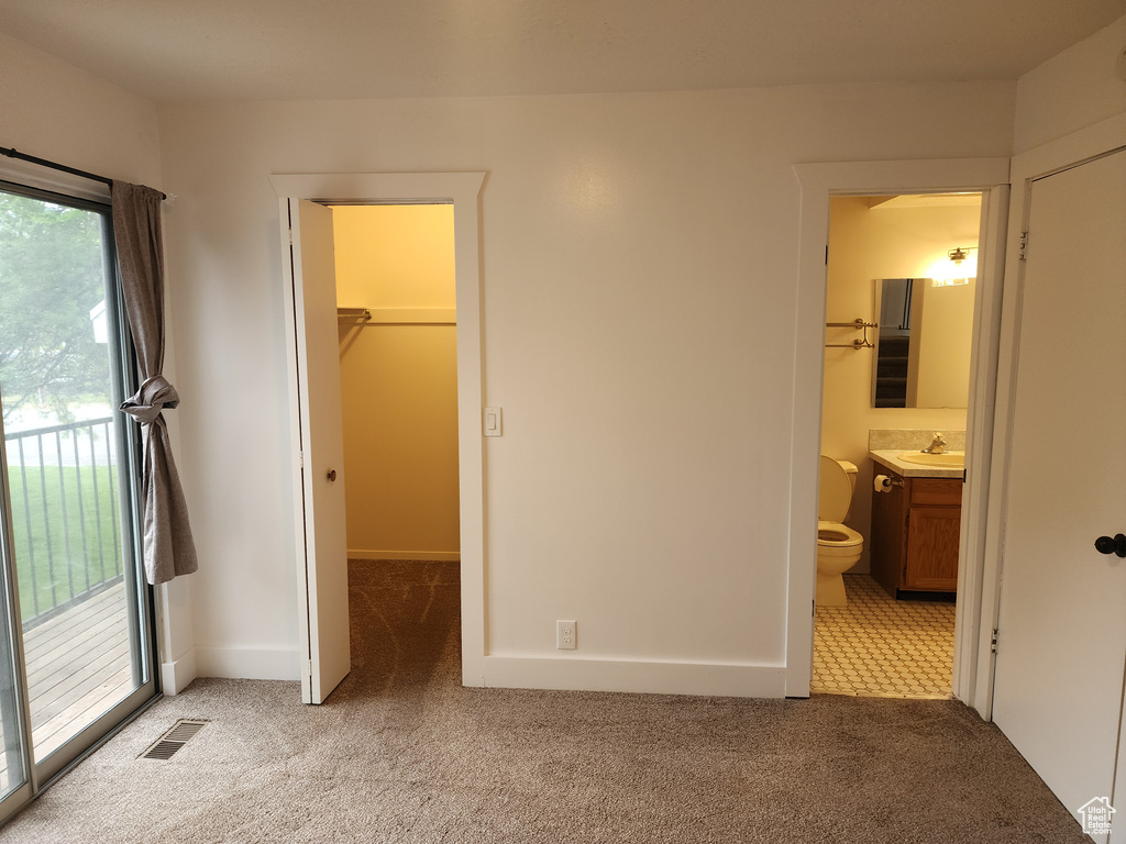 Unfurnished bedroom featuring a sink, light carpet, a walk in closet, and ensuite bath